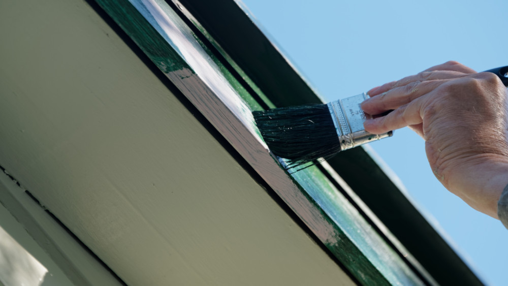 A man painting the trim of a house dark green.